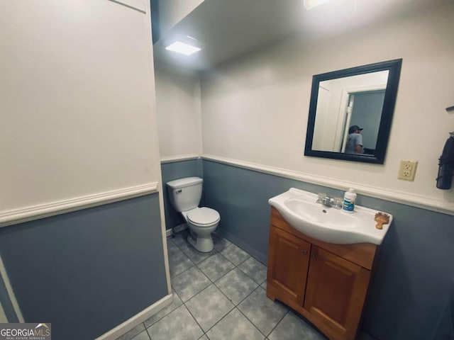 half bath featuring toilet, tile patterned floors, vanity, and baseboards