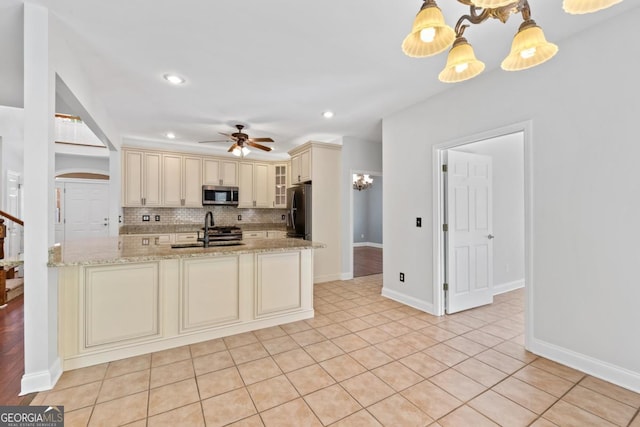kitchen with a sink, ceiling fan with notable chandelier, stainless steel appliances, cream cabinetry, and a peninsula