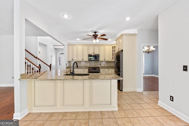 kitchen featuring a sink, black appliances, glass insert cabinets, cream cabinetry, and light stone countertops