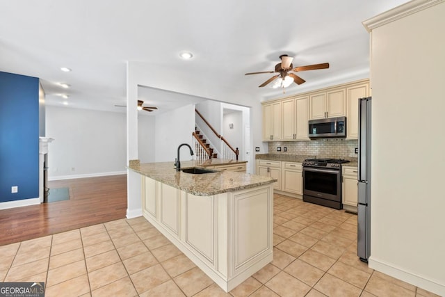 kitchen featuring stainless steel appliances, backsplash, light stone counters, and cream cabinets