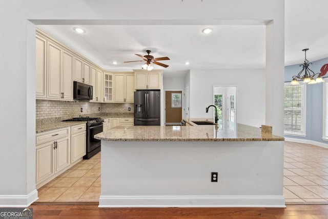kitchen featuring a sink, light tile patterned floors, ceiling fan with notable chandelier, glass insert cabinets, and black appliances