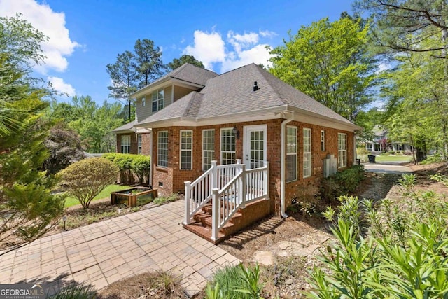 rear view of house featuring brick siding and a shingled roof