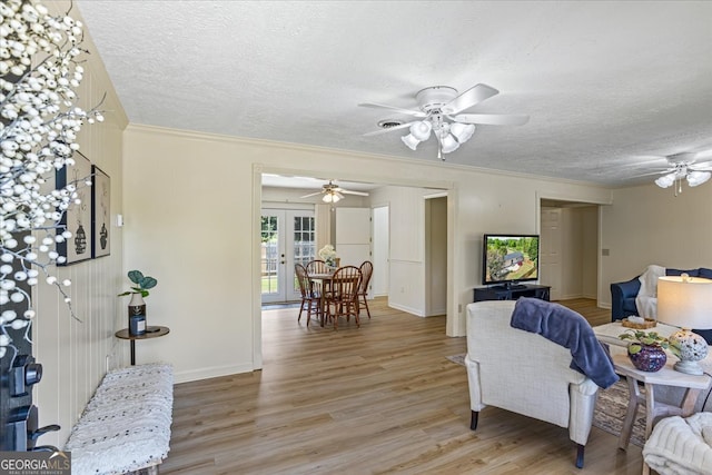 living room with a textured ceiling, ornamental molding, a ceiling fan, french doors, and light wood finished floors
