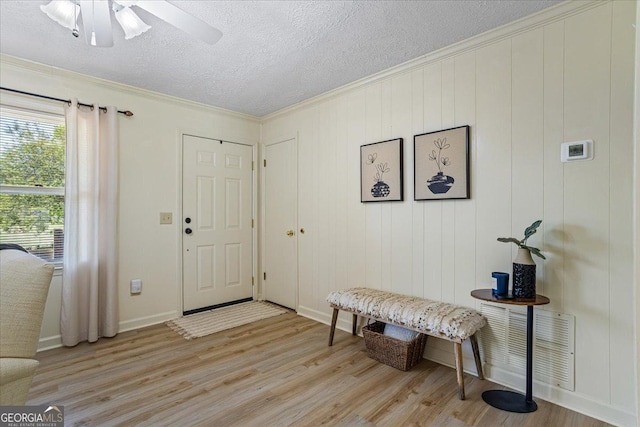 entryway with crown molding, ceiling fan, a textured ceiling, light wood-type flooring, and baseboards