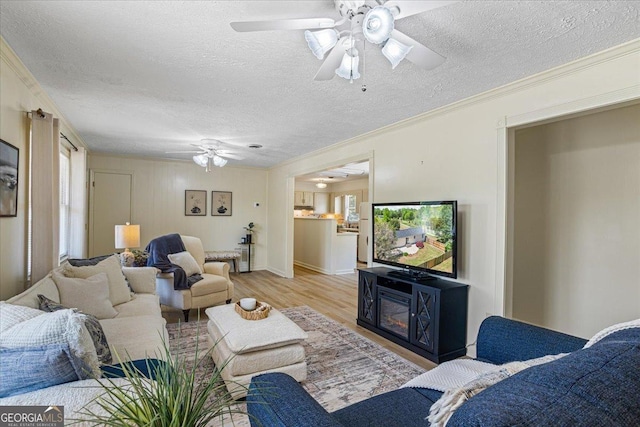 living area with light wood-style flooring, a textured ceiling, ornamental molding, and a ceiling fan