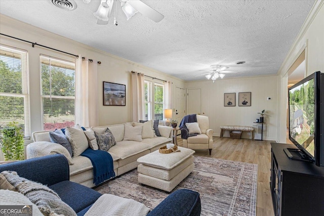 living area with crown molding, visible vents, a ceiling fan, and light wood finished floors