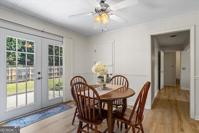 dining room with crown molding, french doors, light wood-type flooring, and a decorative wall