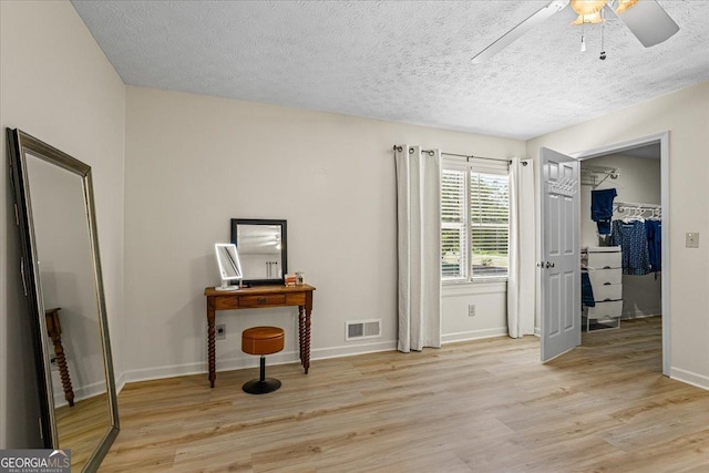 interior space with baseboards, a spacious closet, a textured ceiling, light wood-style floors, and visible vents