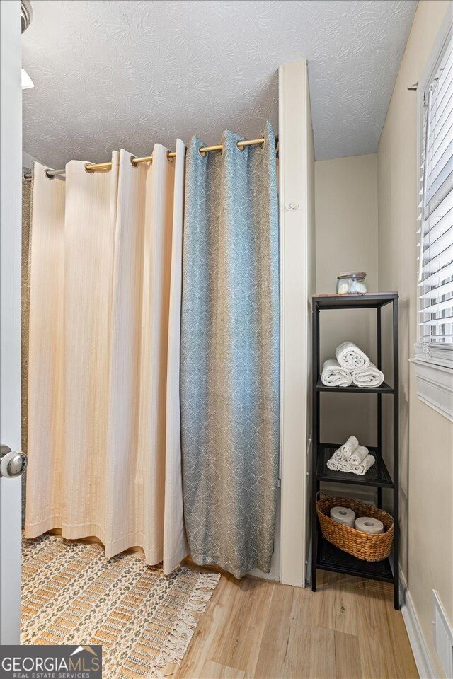 bathroom featuring a textured ceiling, wood finished floors, visible vents, and a healthy amount of sunlight
