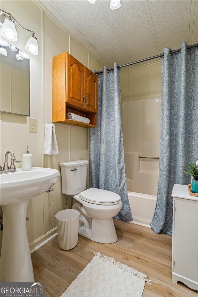 bathroom featuring shower / bathtub combination with curtain, toilet, and wood finished floors