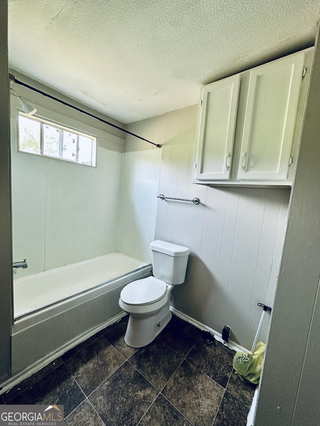 4199 Wagon Trl, Loganville, GA 30052 - bathroom featuring baseboards, toilet, stone finish floor, a textured ceiling, and bathtub / shower combination