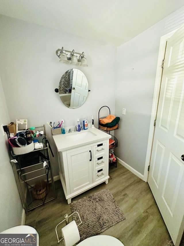 half bath featuring toilet, vanity, wood finished floors, and baseboards