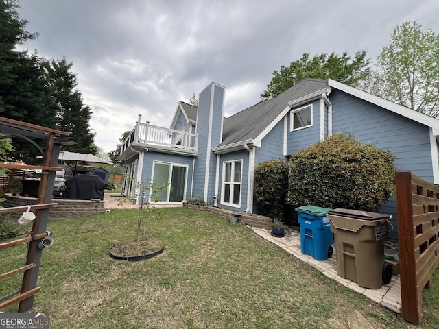 back of property featuring a yard, a balcony, and a chimney