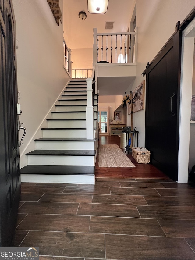 staircase with visible vents, wood finish floors, a barn door, and a high ceiling
