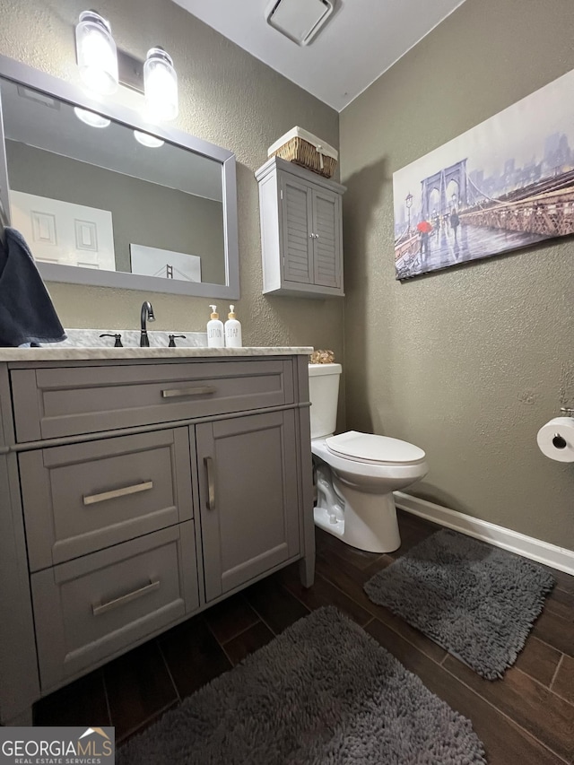 bathroom with toilet, wood finish floors, a textured wall, and baseboards