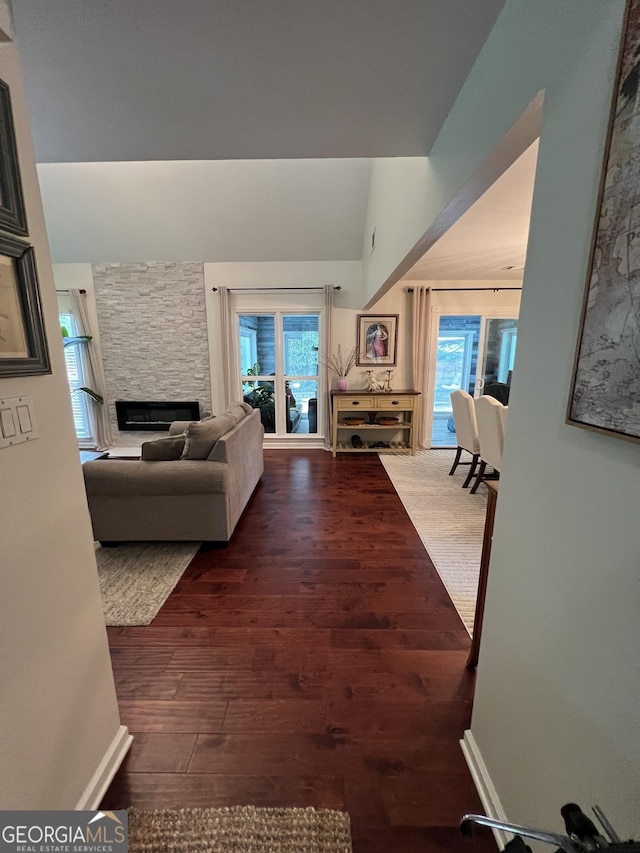 living room featuring a stone fireplace, baseboards, and wood finished floors