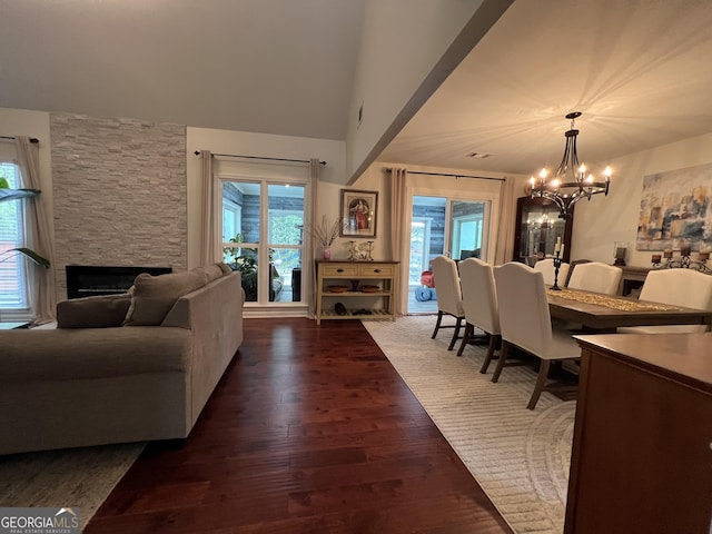 living area with an inviting chandelier, dark wood-style floors, and a stone fireplace