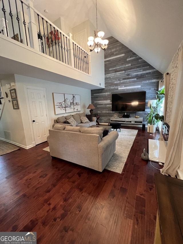 living area with dark wood-style flooring, high vaulted ceiling, an inviting chandelier, and an accent wall
