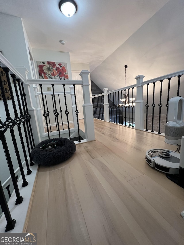 staircase with vaulted ceiling, a notable chandelier, and wood finished floors