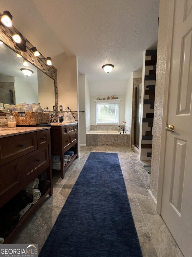 bathroom featuring baseboards, stone finish floor, a textured ceiling, vanity, and a garden tub