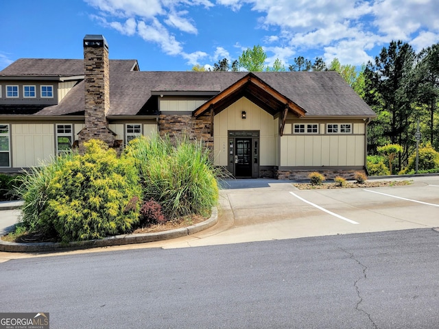 view of front of house with board and batten siding, a shingled roof, and uncovered parking