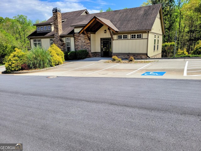 view of front of property with uncovered parking, stone siding, a chimney, and a shingled roof