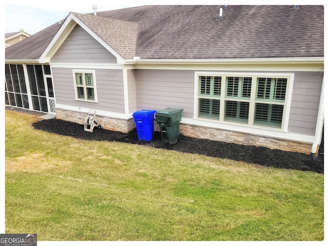 rear view of property with a sunroom, stone siding, a lawn, and a shingled roof