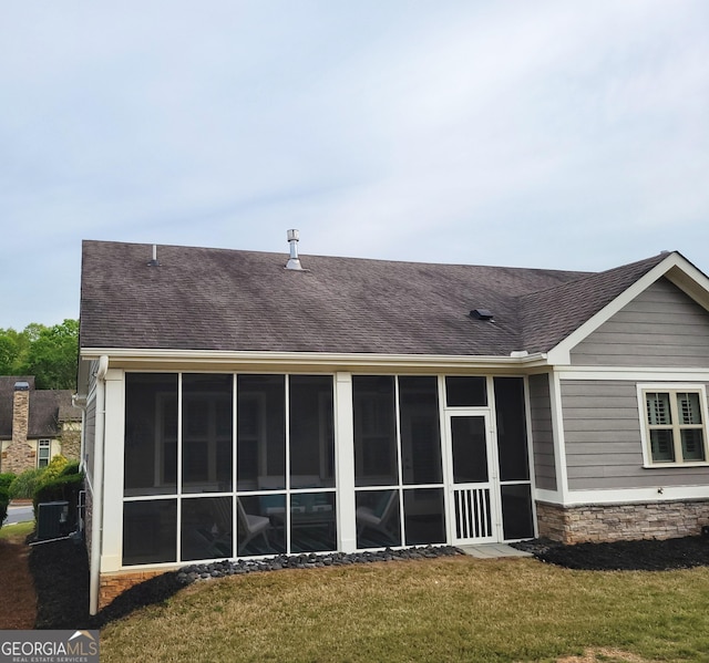 rear view of property with stone siding, a shingled roof, a yard, cooling unit, and a sunroom