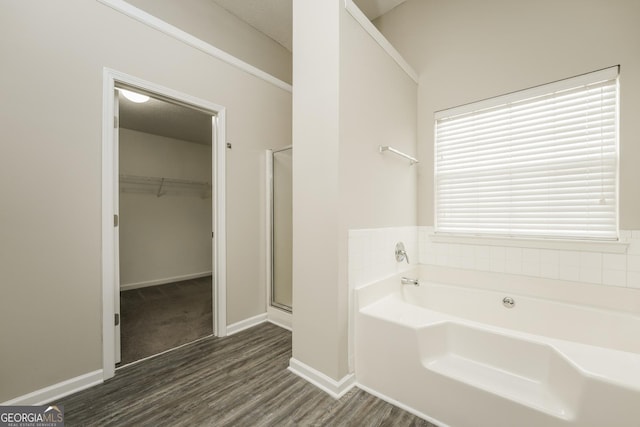 bathroom featuring baseboards, a stall shower, a walk in closet, a garden tub, and wood finished floors