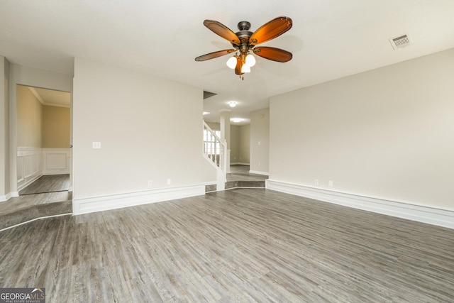spare room featuring stairway, a wainscoted wall, visible vents, ceiling fan, and wood finished floors