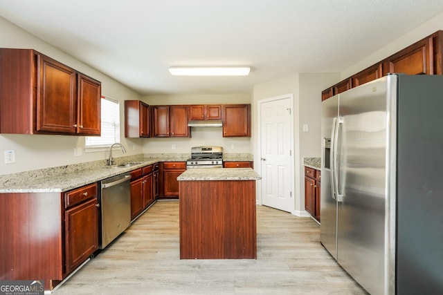 kitchen with a kitchen island, under cabinet range hood, stainless steel appliances, light wood finished floors, and a sink