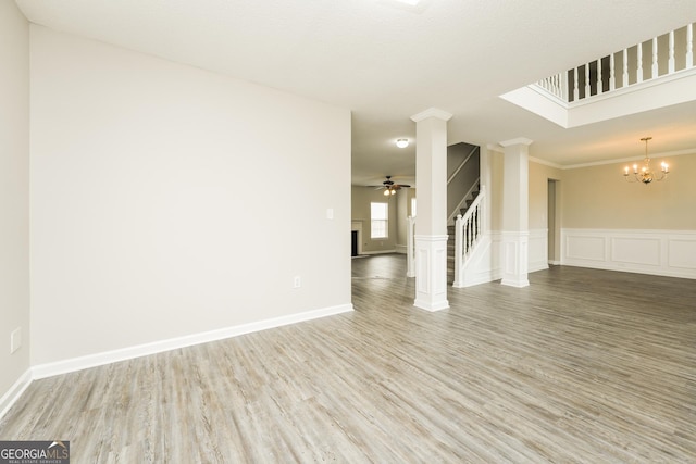 spare room with crown molding, stairway, wainscoting, wood finished floors, and ceiling fan with notable chandelier