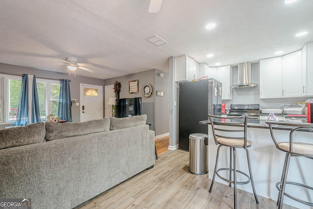 kitchen with ceiling fan, a textured ceiling, wall chimney range hood, appliances with stainless steel finishes, and open floor plan