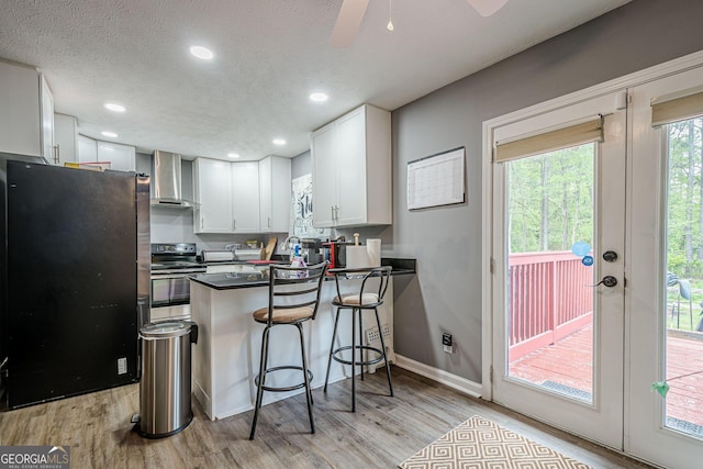 kitchen with light wood-type flooring, wall chimney exhaust hood, electric range, and freestanding refrigerator