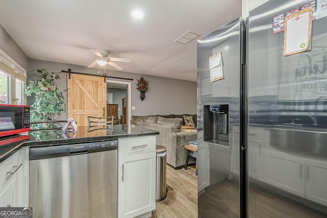 kitchen with ceiling fan, visible vents, a barn door, appliances with stainless steel finishes, and dark countertops