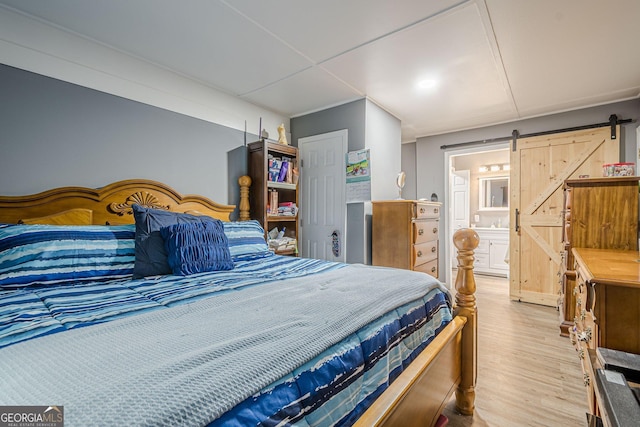 bedroom with ensuite bathroom, a barn door, and light wood-style floors