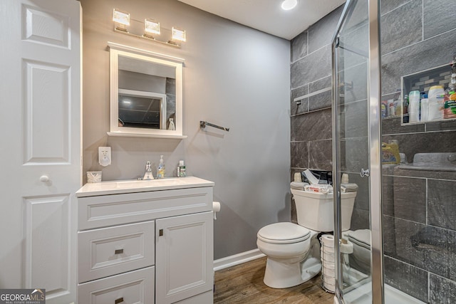 bathroom with vanity, toilet, wood finished floors, a stall shower, and baseboards