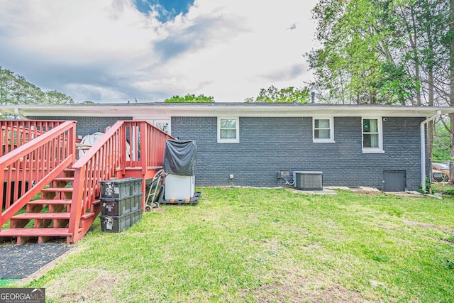 rear view of house featuring a yard, brick siding, cooling unit, and a wooden deck