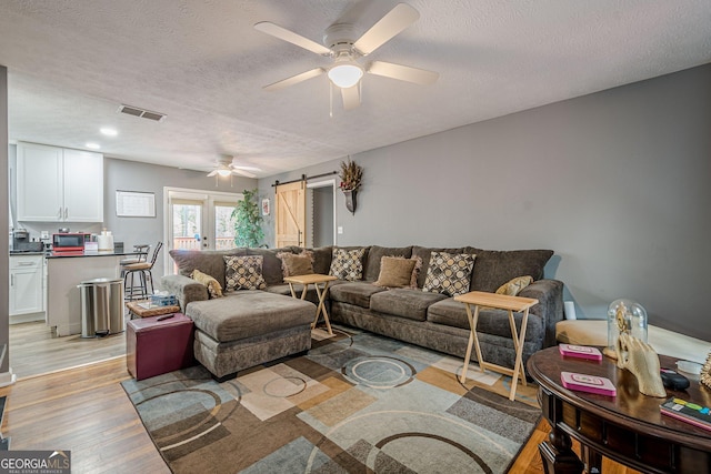 living area with visible vents, a barn door, ceiling fan, light wood-type flooring, and a textured ceiling