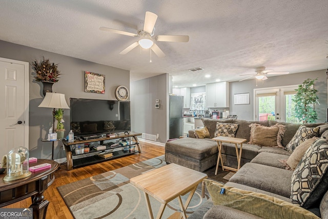 living room featuring visible vents, a ceiling fan, light wood-style floors, and a textured ceiling