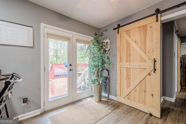 doorway with a ceiling fan, visible vents, a barn door, wood finished floors, and baseboards