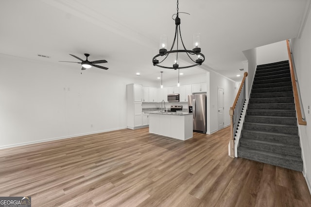 unfurnished living room with visible vents, light wood finished floors, recessed lighting, ceiling fan with notable chandelier, and stairs