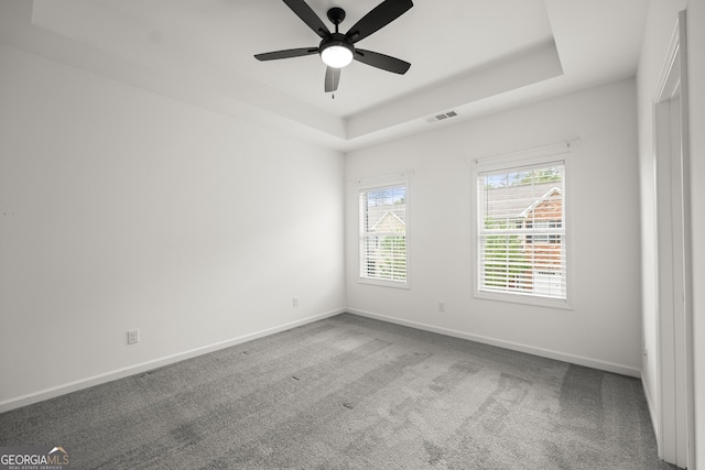 carpeted spare room with visible vents, baseboards, a raised ceiling, and ceiling fan