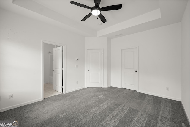 unfurnished bedroom with carpet, a tray ceiling, ensuite bath, visible vents, and baseboards