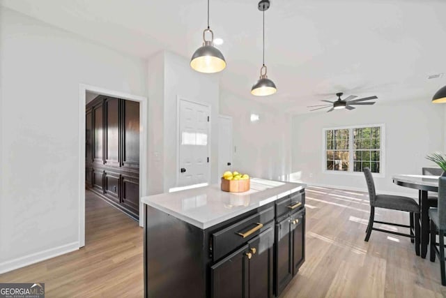 kitchen featuring light wood-style floors, decorative light fixtures, light countertops, a kitchen island, and a ceiling fan