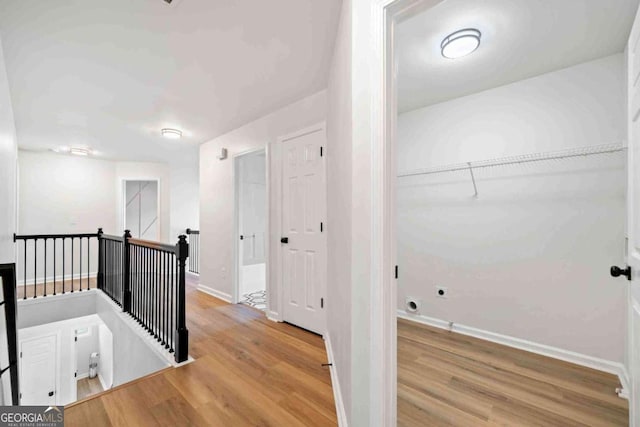hall featuring an upstairs landing, wood finished floors, and baseboards