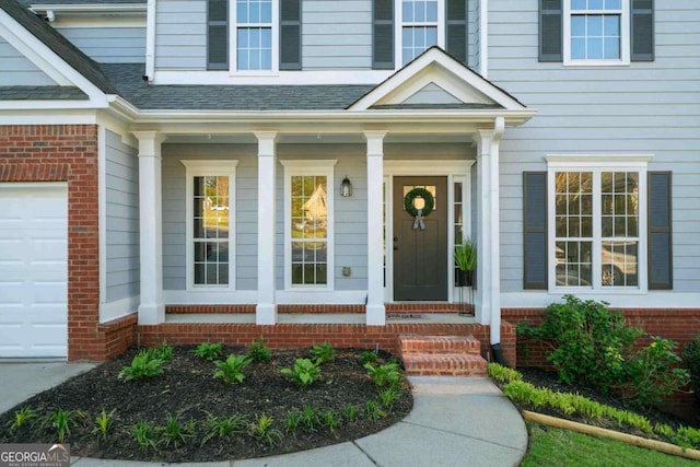 view of exterior entry featuring covered porch, a shingled roof, and brick siding