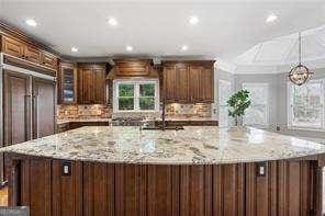kitchen with a large island, paneled fridge, decorative backsplash, and light stone countertops
