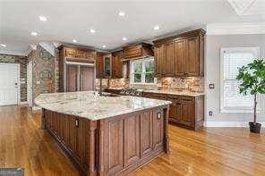 kitchen with refrigerator, baseboards, recessed lighting, a center island with sink, and light wood finished floors