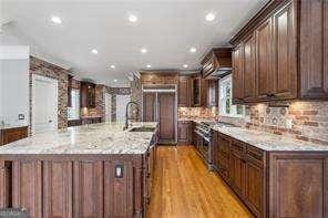 kitchen with a large island with sink, light stone countertops, dark brown cabinets, recessed lighting, and a sink